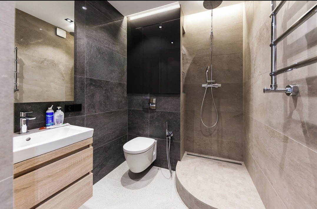 Nowoczesna łazienka z kabiną typu walk-in, szarymi płytkami imitującymi kamień i drewnianą szafką pod umywalką. Minimalistyczny design, oświetlenie LED.