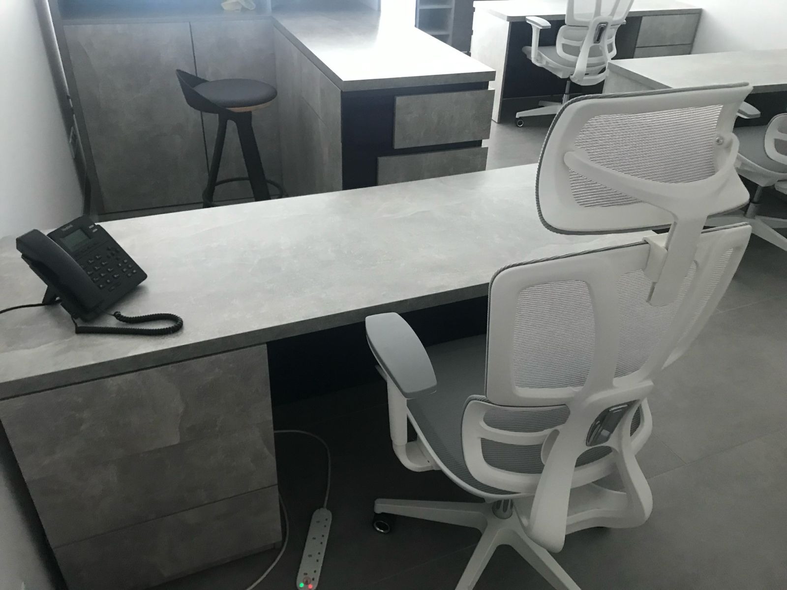 Nowoczesne biuro z szarymi biurkami, krzesłami z siatki i telefonem stacjonarnym. Minimalistyczny design z akcentem na funkcjonalność i ergonomię.