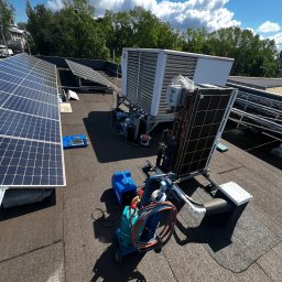 WM POMPY CIEPŁA I KLIMATYZACJA - Instalacja fotowoltaiczna na dachu budynku z zamontowaną jednostką klimatyzacyjną i narzędziami serwisowymi. Widok z góry, słoneczny dzień.