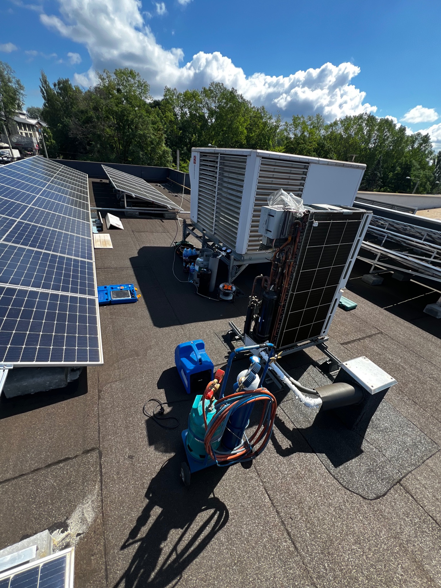 Instalacja fotowoltaiczna na dachu budynku z zamontowaną jednostką klimatyzacyjną i narzędziami serwisowymi. Widok z góry, słoneczny dzień.