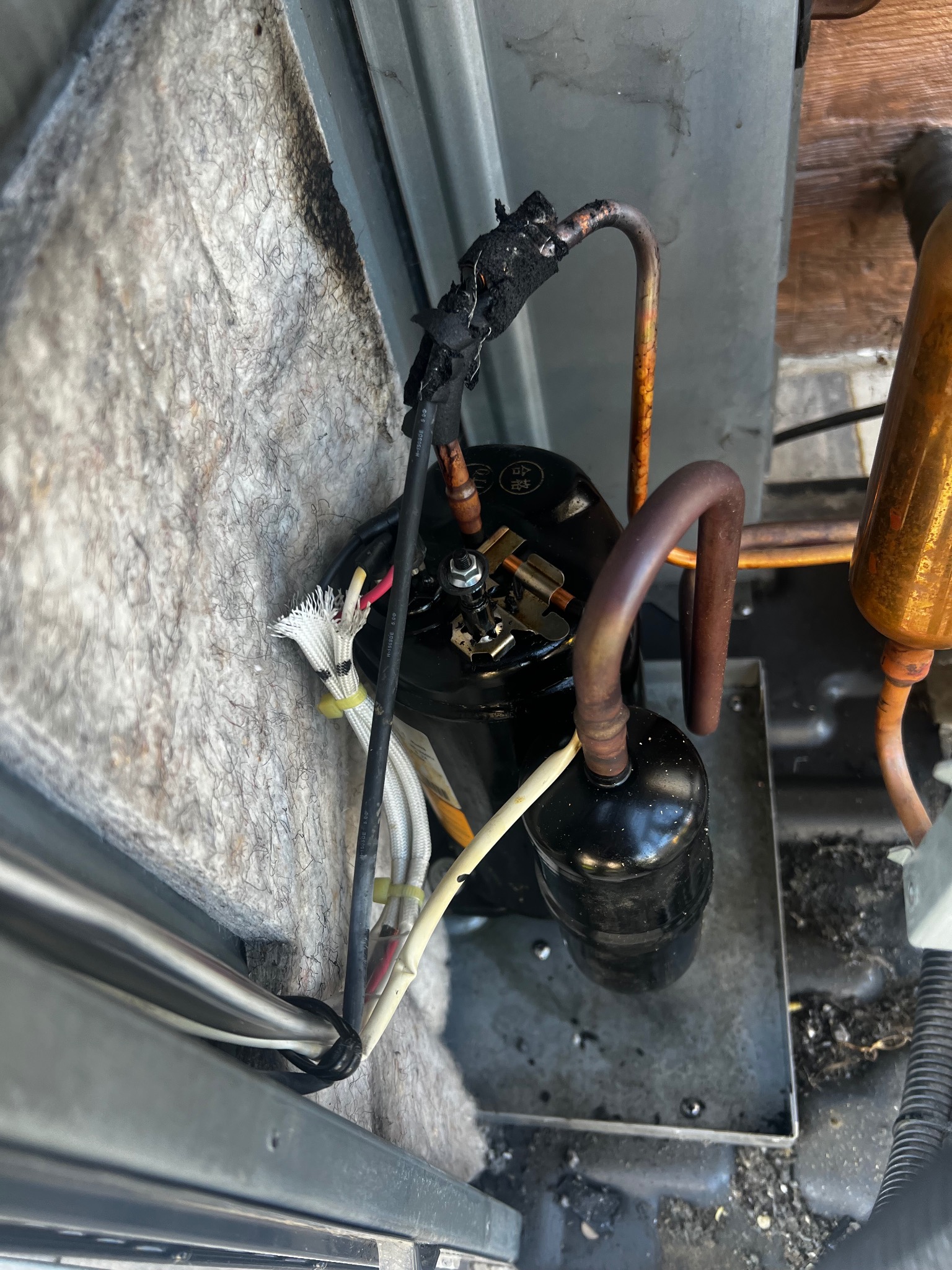 Uszkodzony kompresor klimatyzacji z widocznymi przewodami i rurkami, prawdopodobnie po awarii. Widoczne ślady przepalenia na izolacji przewodów.