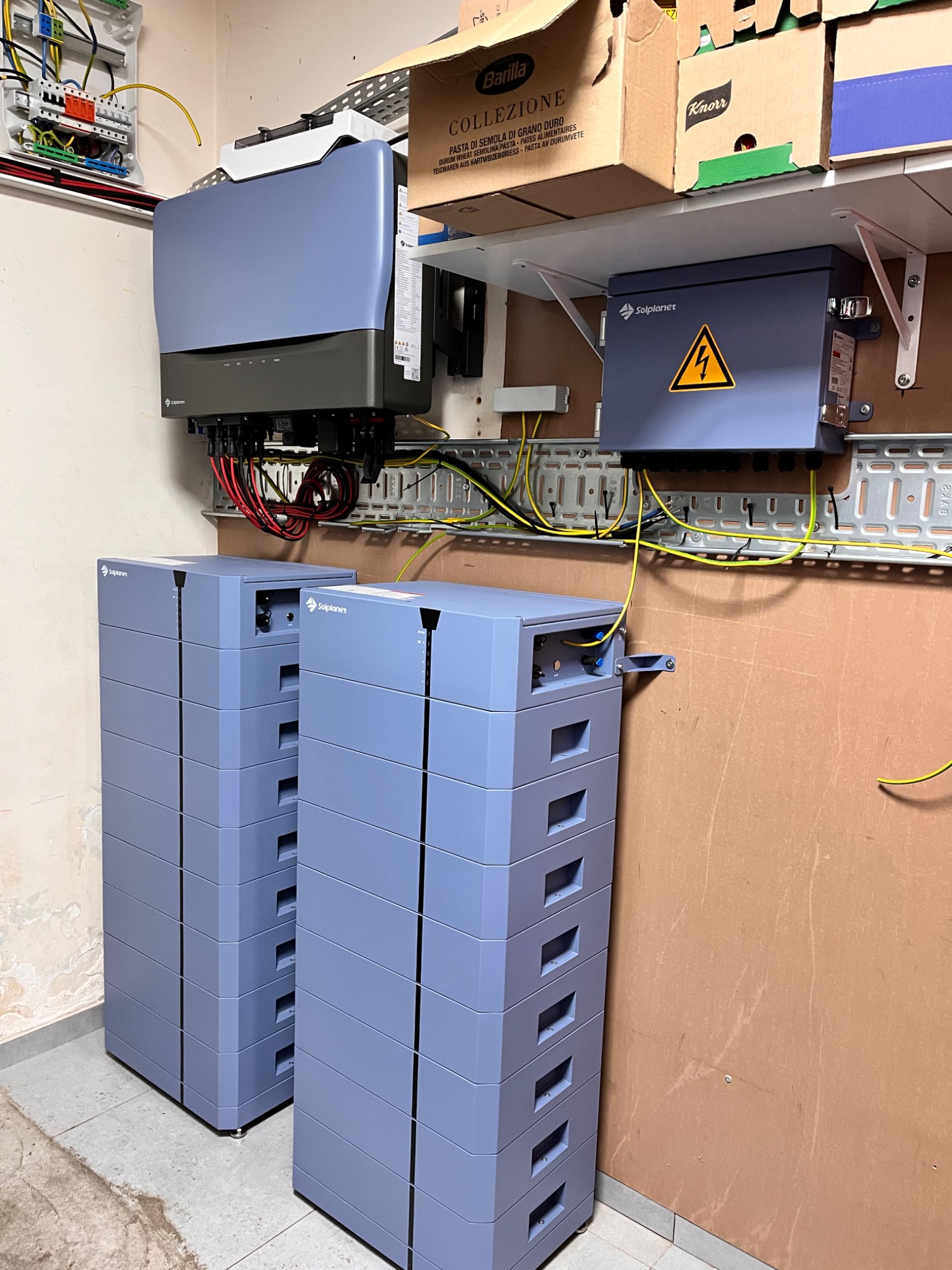 Kompletna instalacja magazynu energii Solplanet z falownikiem i modułami bateryjnymi, zamontowana na ścianie z widocznymi przewodami i elementami zabezpieczeń.