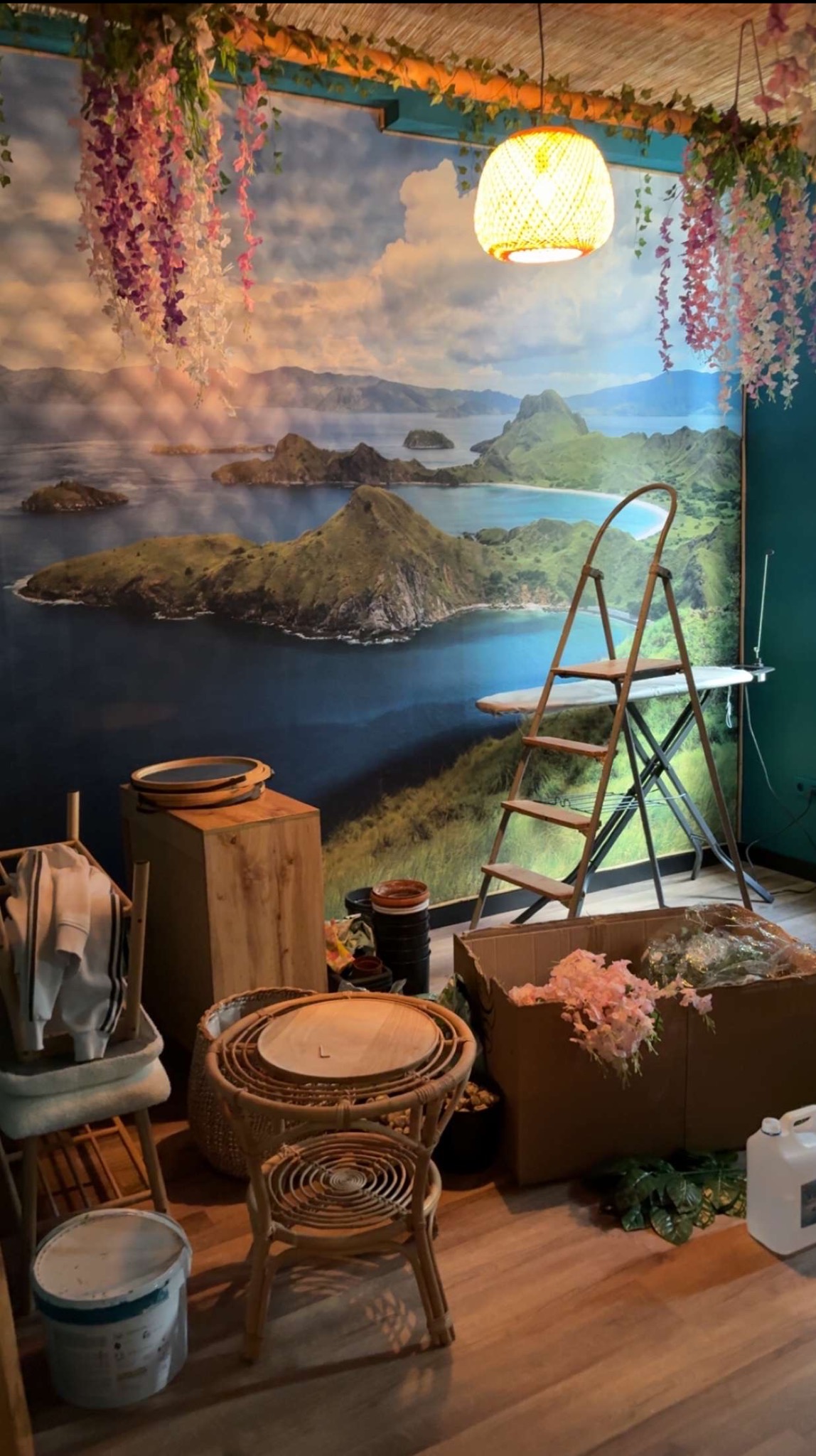 Pokój w trakcie dekorowania z fototapetą górskiego krajobrazu, drabina oparta o ścianę, rekwizyty dekoracyjne, lampa wisząca i drewniana podłoga. Przygotowania do sesji zdjęciowej.