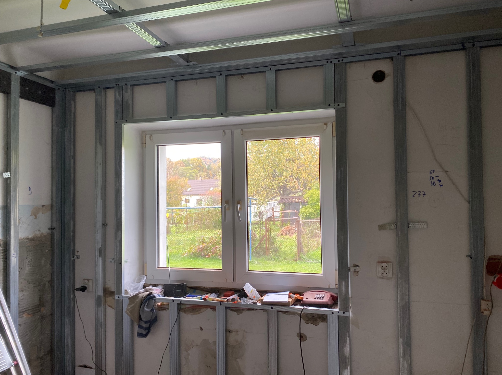 Montaż metalowej konstrukcji pod płyty gipsowo-kartonowe wokół okna. Widoczne profile, narzędzia i instalacje. Etap prac wykończeniowych w pomieszczeniu.