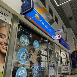 Biuro Podróży Ole Travel - salon podróży - Fasada biura podróży Coral Travel w galerii handlowej, z logo i ofertami wycieczek na szybach. Widoczne loga innych biur: Grecos, Itaka, Rainbow Tours.