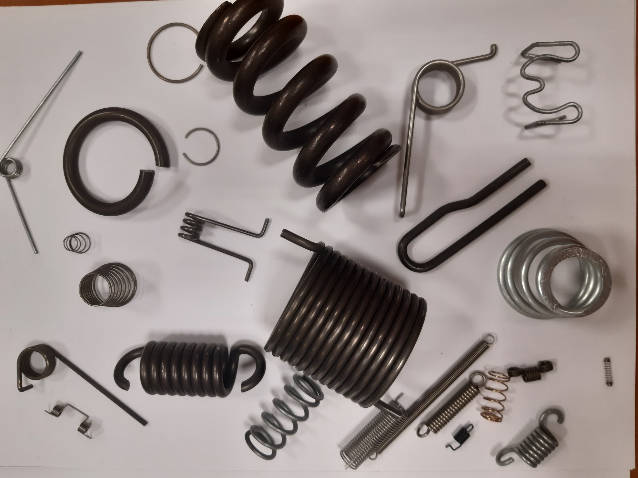 Różnorodne sprężyny: ściskane, naciągowe, skrętne, pierścieniowe i spiralne, ułożone na białym tle. Elementy metalowe o różnych rozmiarach i kształtach.