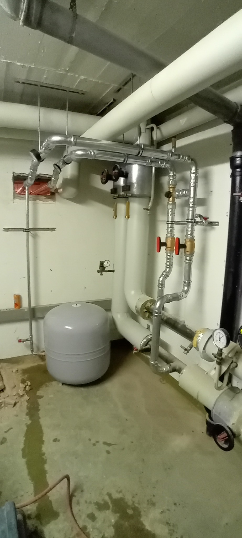 Złożona instalacja grzewcza z rurami, zaworami i zbiornikiem wyrównawczym w kotłowni. Widoczne manometry i elementy mocujące. Realizacja instalacji w piwnicy.