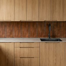 Magda Sikorska AMMA studio - Nowoczesna kuchnia z drewnianymi szafkami o minimalistycznym designie i brązowym panelem nad blatem. Czarny zlew i bateria dodają elegancji.