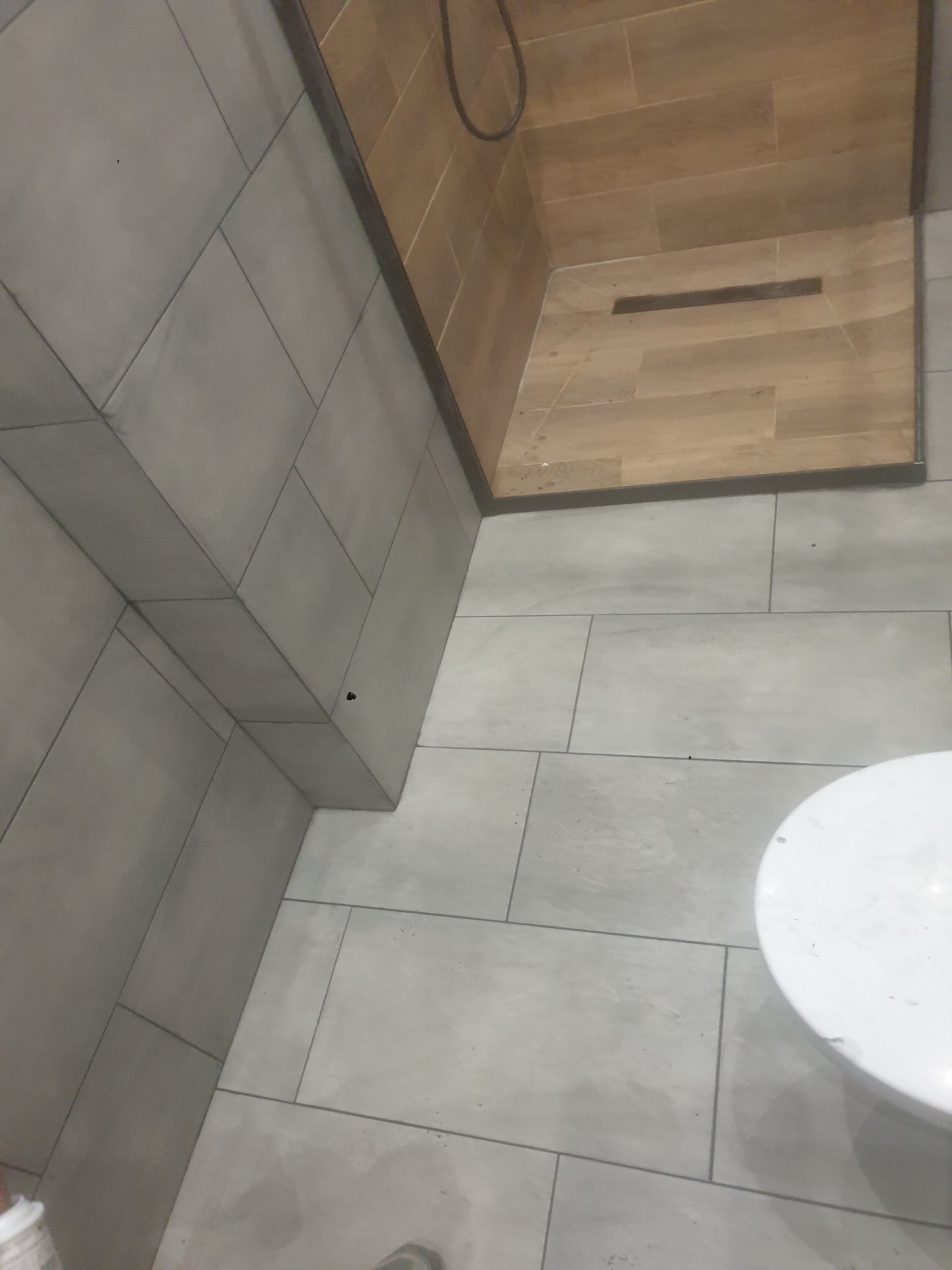 Nowoczesna łazienka z szarymi płytkami na ścianach i podłodze, kabina prysznicowa z drewnopodobnymi płytkami i odpływem liniowym. Minimalistyczny design.