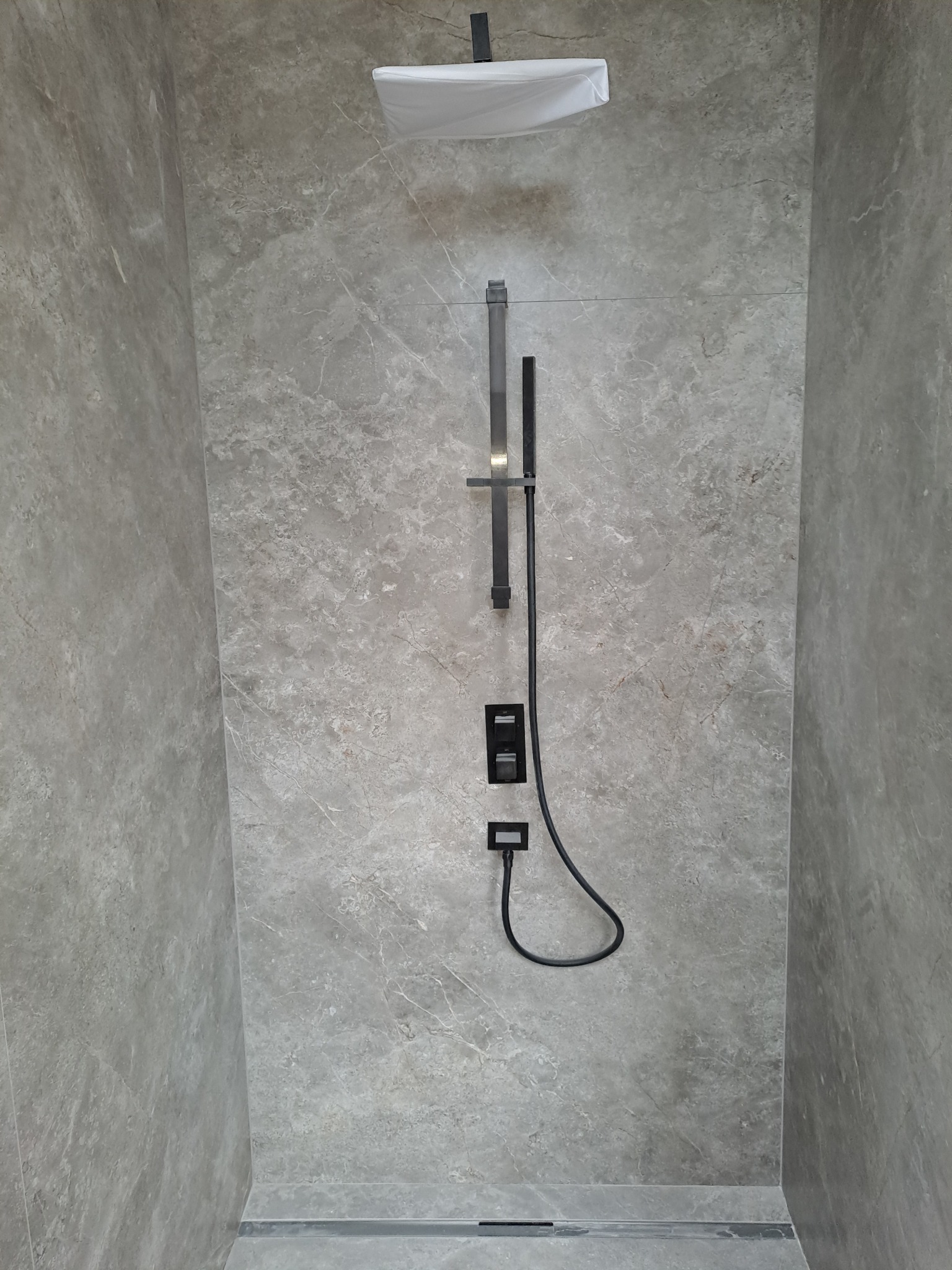 Nowoczesna kabina prysznicowa z szarymi płytkami imitującymi marmur, czarną armaturą i odpływem liniowym. Minimalistyczny design, eleganckie wykończenie.