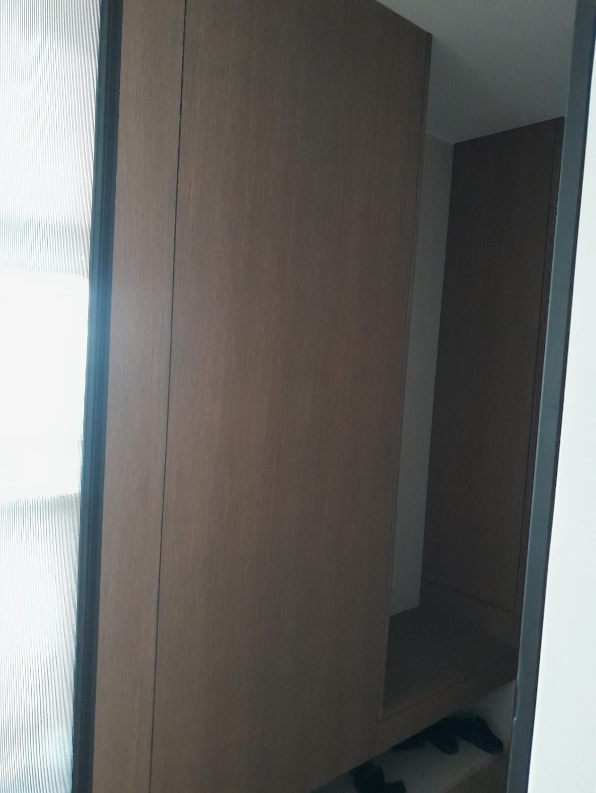 Drewniana szafa wnękowa z półkami, widoczna z boku, z minimalistycznym wykończeniem i subtelnym oświetleniem wewnątrz. Ciemne wykończenie ramy drzwi.