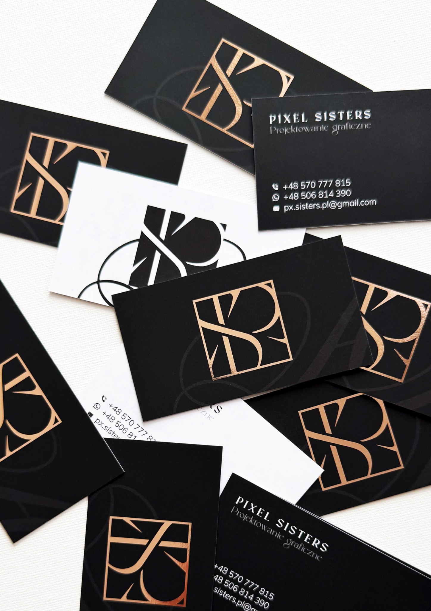 Eleganckie wizytówki Pixel Sisters z logo w kolorze złota na czarnym tle, ułożone warstwami. Minimalistyczny design, profesjonalny wygląd, detale kontaktowe widoczne.