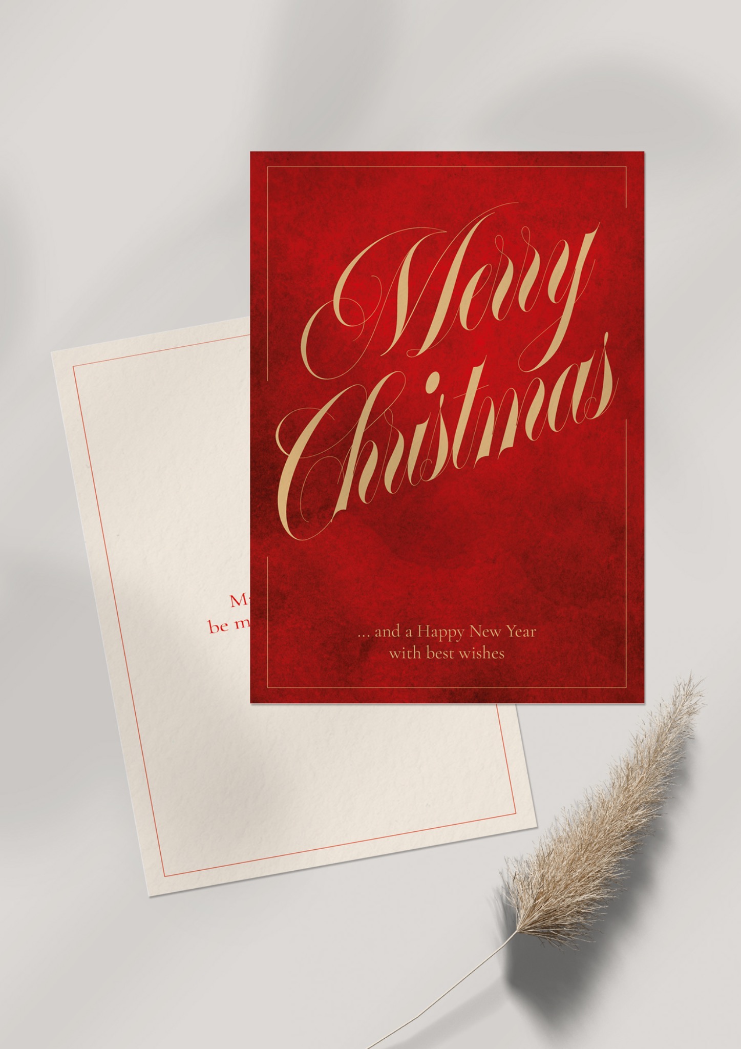 Elegancka kartka świąteczna w odcieniach czerwieni i złota z napisem 'Merry Christmas' oraz życzeniami noworocznymi, obok pusta kartka i źdźbło trawy.