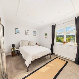 siemieniagos - Jasna sypialnia z łóżkiem, dywanem i dużym lustrem w ozdobnej ramie. Widok na zieleń za oknem. Minimalistyczny wystrój z plakatami na ścianie.