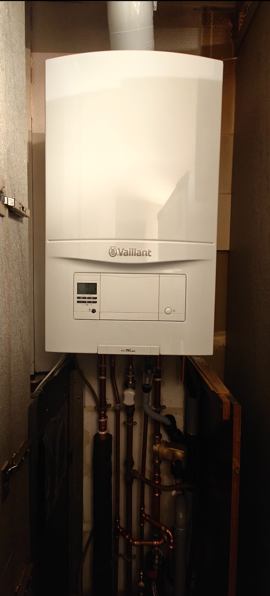 Biały piec gazowy Vaillant EcoTEC pro z widocznymi rurami miedzianymi w zabudowie. Ujęcie z dołu, widoczne elementy instalacji.