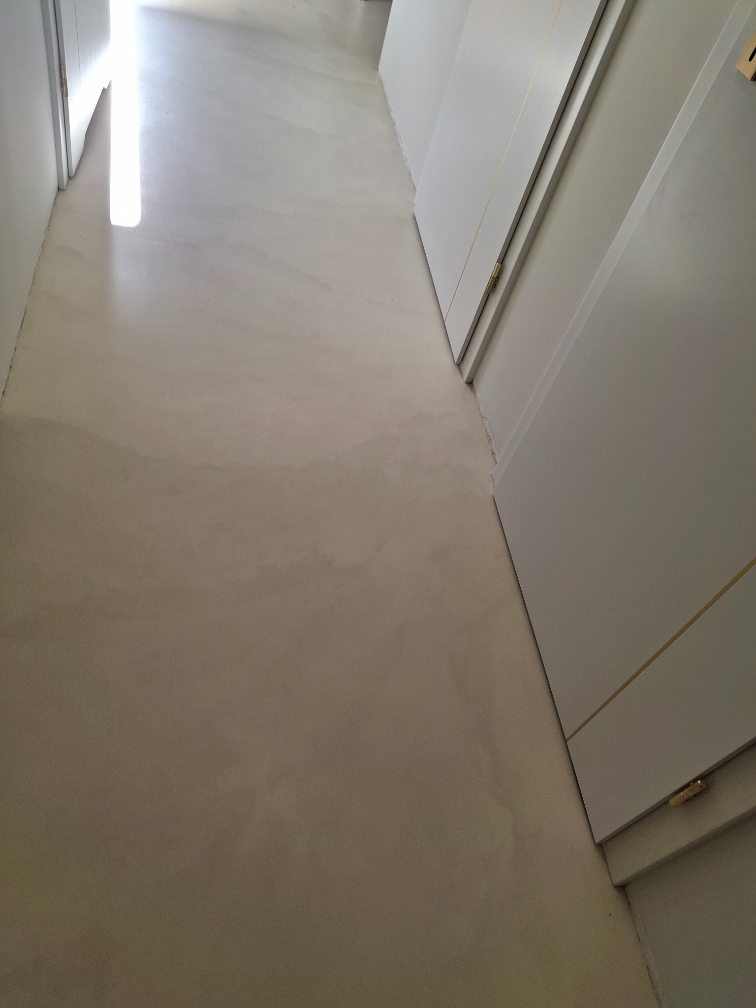 Jasna, gładka posadzka w korytarzu, z widocznym efektem polerowania i subtelnymi przejściami tonalnymi. Białe drzwi po prawej stronie kadru.