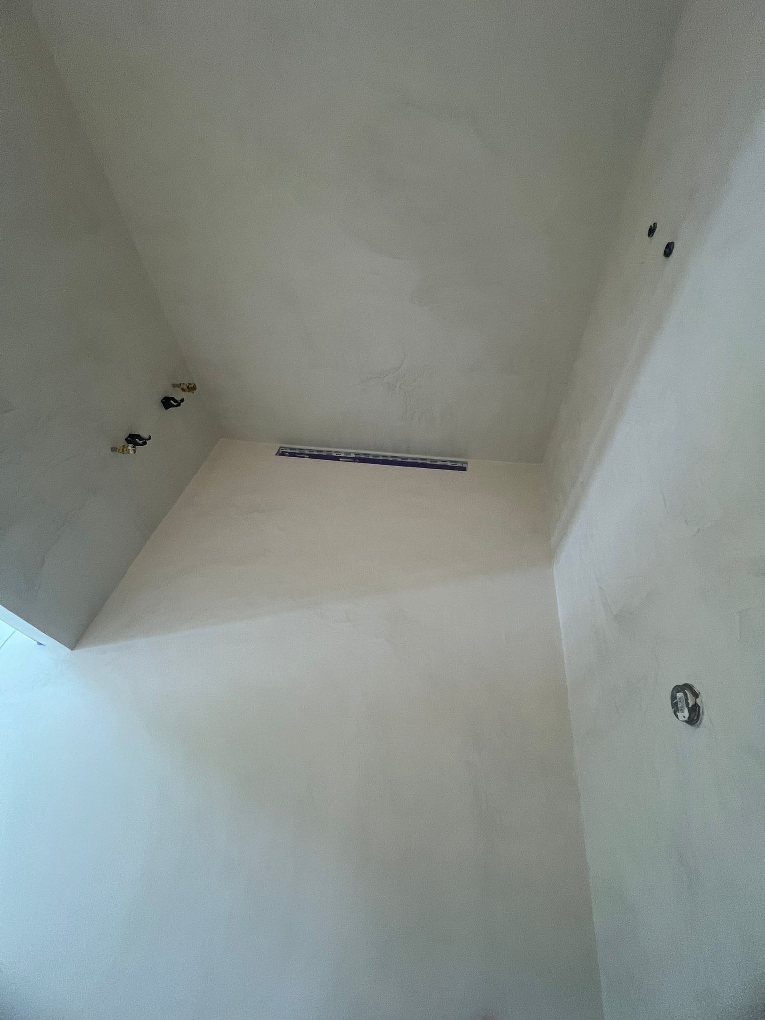 Wnętrze po gładziowaniu ścian i sufitu, widoczne otwory instalacyjne i odpływ liniowy. Ściany w jasnym odcieniu, gotowe do dalszych prac wykończeniowych.