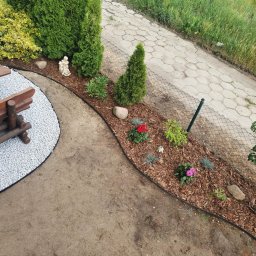 Patryk Żołnowski - Aranżacja ogrodu z rabatą kwiatową, obrzeżem i ścieżką z białego żwiru. W tle widoczny chodnik z kostki i fragment ogrodzenia z siatki.