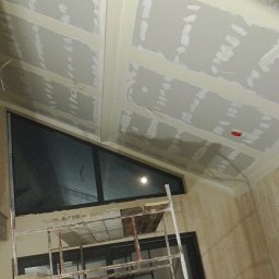 Artur Dąbek - Sufit z płyt karton-gips, częściowo wyszpachlowany, widoczne łączenia. Okno trójkątne w czarnej ramie. Fragment rusztowania. Prace wykończeniowe wnętrza.