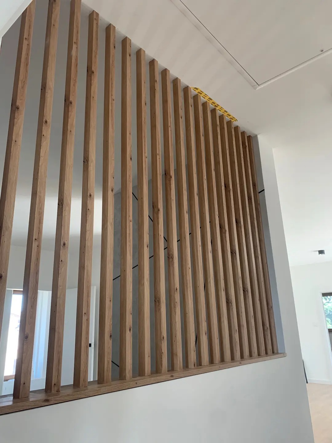 Drewniana ażurowa ścianka działowa, pionowe listwy z naturalnego drewna, nowoczesny design wnętrza w Rawa Mazowiecka, białe ściany, minimalistyczny styl.