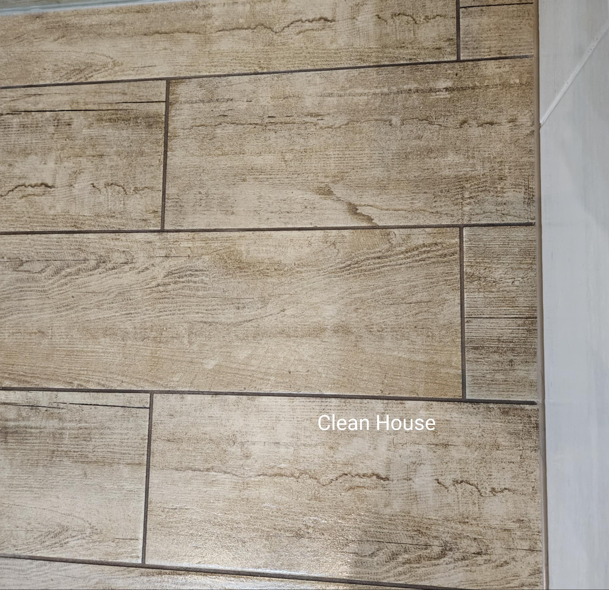 Ukończona podłoga z płytek imitujących drewno w odcieniach beżu i brązu, po profesjonalnym czyszczeniu. Widoczna fuga i fragment ściany.