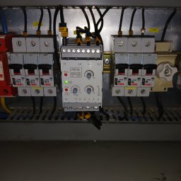 EI-ELEKTRYK Sp. z o.o. - Szczegółowe ujęcie rozdzielnicy elektrycznej z bezpiecznikami FAEL i modułem PKF5e, widoczne przewody i oznaczenia. Oświetlenie górne.