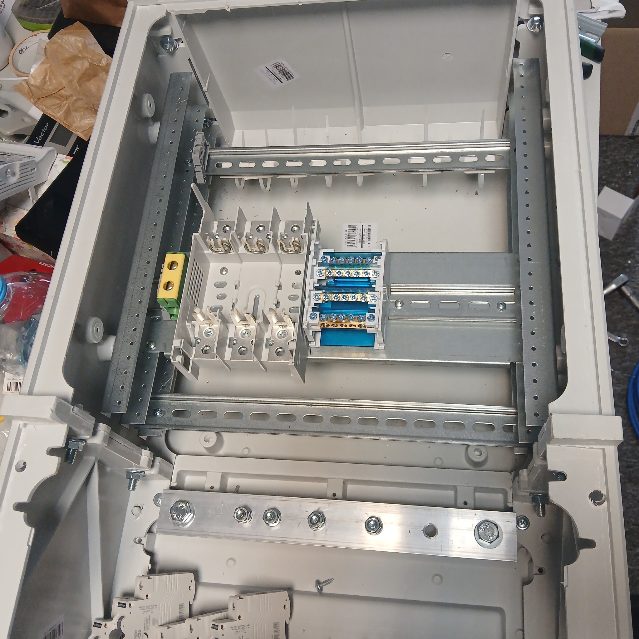 Wnętrze rozdzielnicy elektrycznej w trakcie montażu, widoczne szyny DIN, listwy zaciskowe i zabezpieczenia. Elementy zamocowane w białej obudowie.