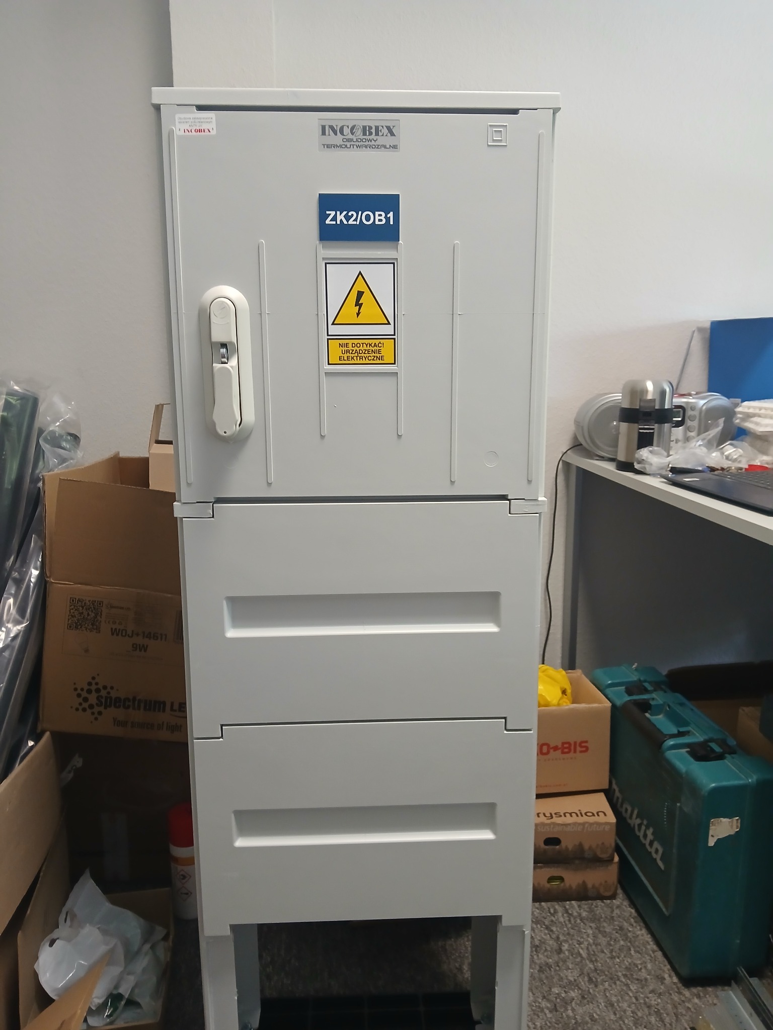 Szara szafa elektryczna IncoBex ZK2/OB1 z ostrzeżeniem o napięciu, widoczna w Białymstoku. Obok kartony i narzędzia, co sugeruje etap instalacji lub konserwacji.