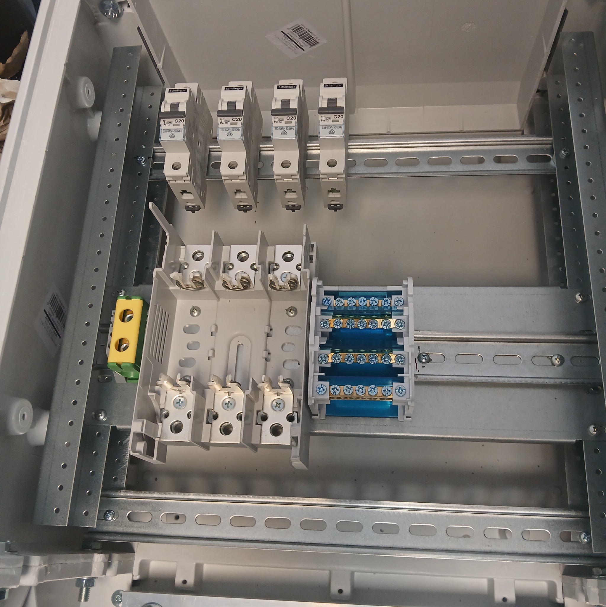 Rozdzielnica elektryczna w trakcie montażu: widoczne zabezpieczenia C20, listwy zaciskowe i szyny montażowe wewnątrz obudowy. Detal instalacji elektrycznej.
