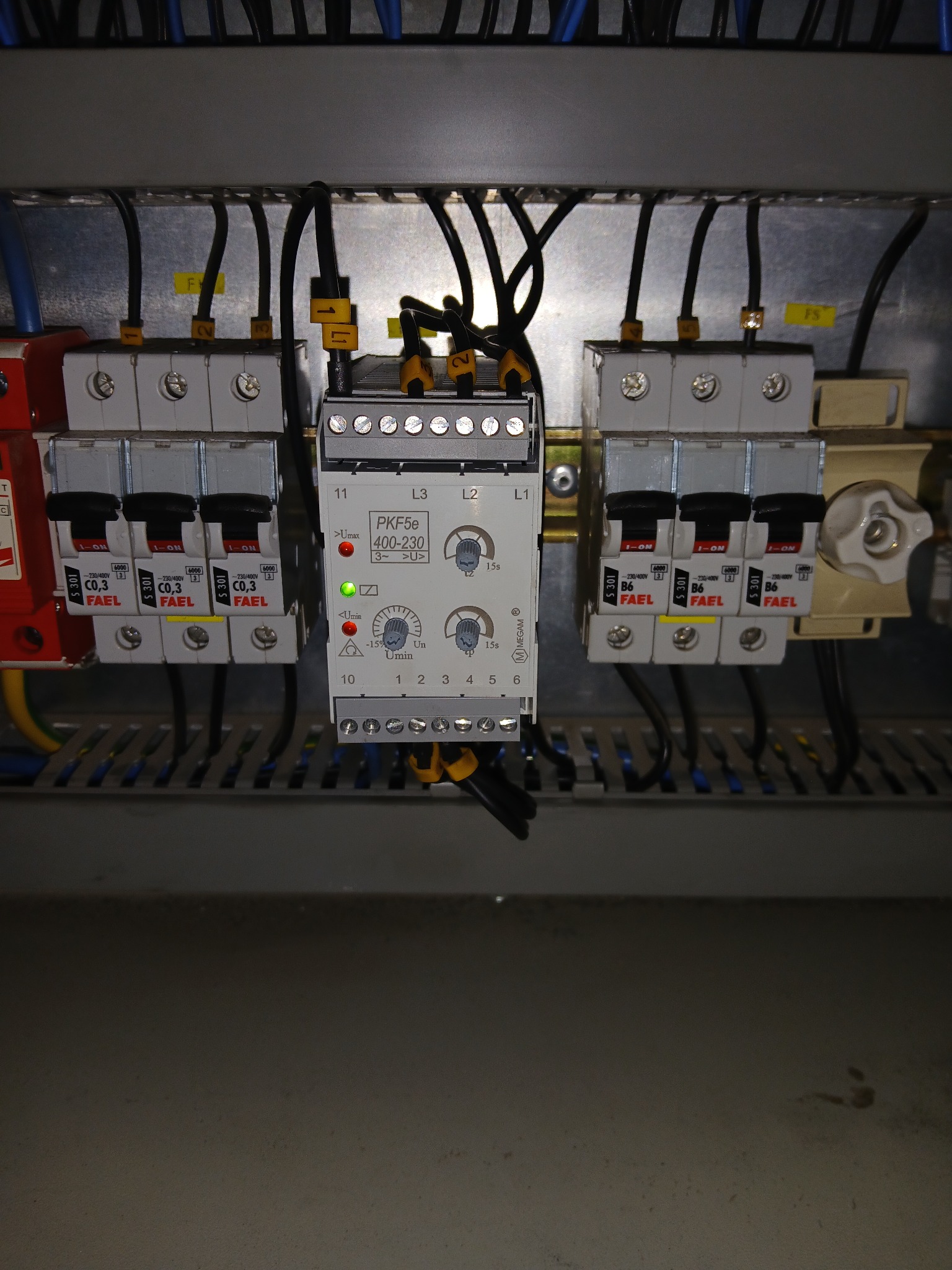 Szczegółowe ujęcie rozdzielnicy elektrycznej z bezpiecznikami FAEL i modułem PKF5e, widoczne przewody i oznaczenia. Oświetlenie górne.