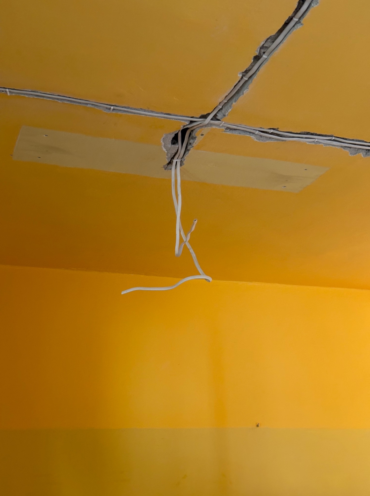 Żółte wnętrze w trakcie remontu: kable elektryczne wystające z sufitu, widoczne bruzdy z przewodami i fragment łatki na suficie. Prace instalacyjne w toku.