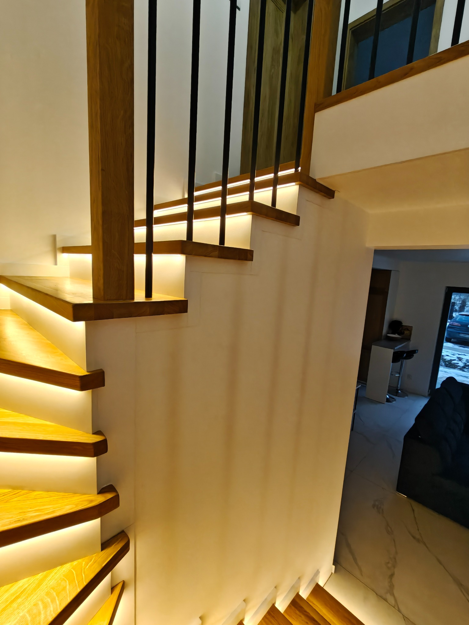 Nowoczesne schody z podświetleniem LED i czarną balustradą w Orzeszu. Drewniane stopnie o ciepłym odcieniu, minimalistyczny design, eleganckie wykończenie.