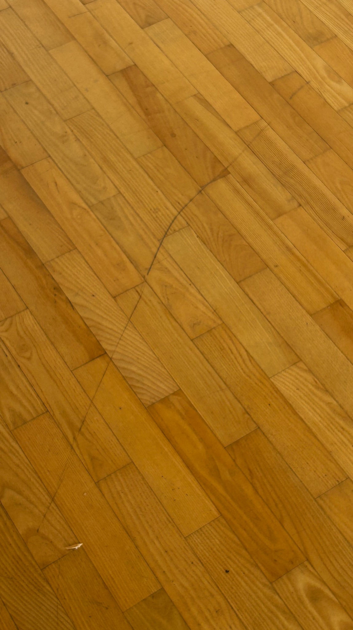 Parkiet z drewna dębowego ułożony pod kątem, widoczna delikatna rysa na powierzchni. Ciepłe oświetlenie podkreśla naturalny rysunek słojów.