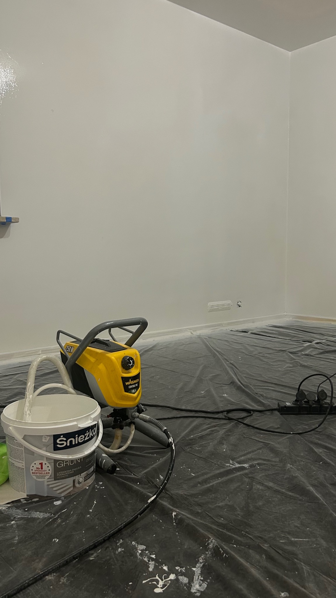 Pokój po gruntowaniu ścian, przygotowany do malowania. Widoczny agregat malarski Wagner, wiadro z gruntem Śnieżka i folia ochronna na podłodze.
