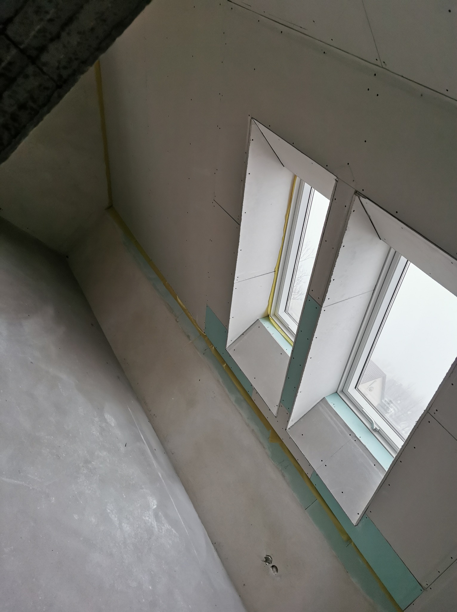 Montaż płyt karton-gips na poddaszu z oknami dachowymi. Widoczne łączenia płyt i szpachlowanie. Surowy stan wykończenia, widok z dołu.