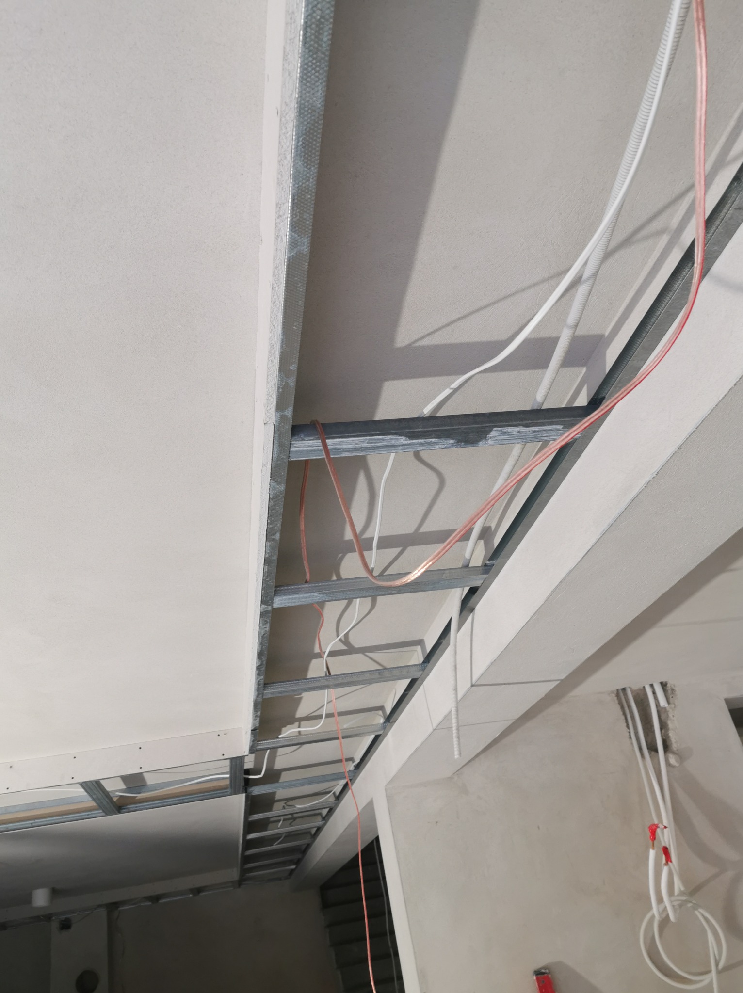 Montaż sufitu podwieszanego z płyt karton-gips na metalowej konstrukcji, widoczne przewody elektryczne. Detal wykończenia wnętrza w trakcie prac.