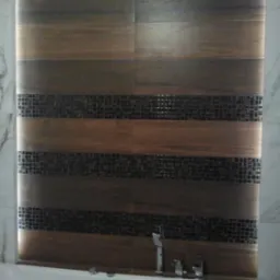 Wykończona ściana łazienki z poziomymi pasami płytek imitujących drewno, oddzielonych paskami mozaiki, oświetlona ledowo po bokach, z widoczną baterią umywalkową i fragmentem wanny.