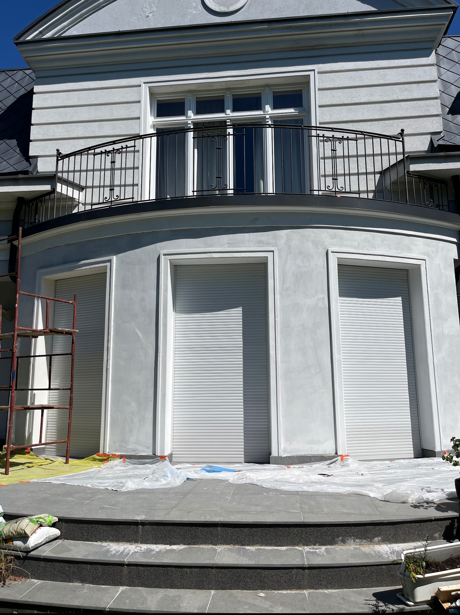 Elewacja budynku po szpachlowaniu i przygotowaniu do malowania. Widoczne rusztowanie, zabezpieczenia folią i worki z materiałami budowlanymi.