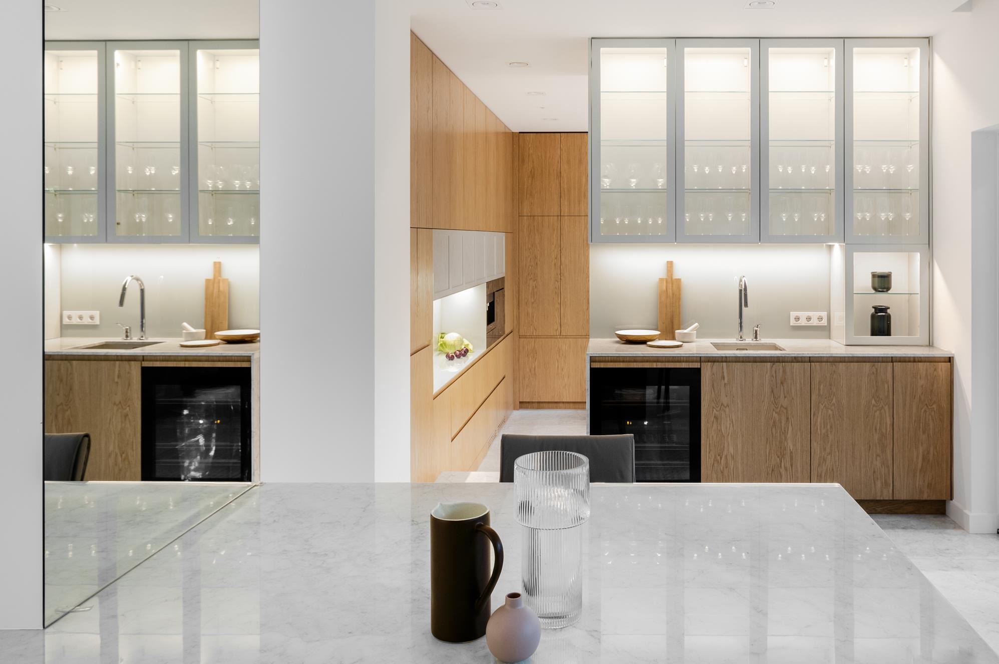 Nowoczesna kuchnia z drewnianymi szafkami i marmurowym blatem w Warszawie. Minimalistyczny design, szklane witryny, oświetlenie LED. Eleganckie wykończenie.