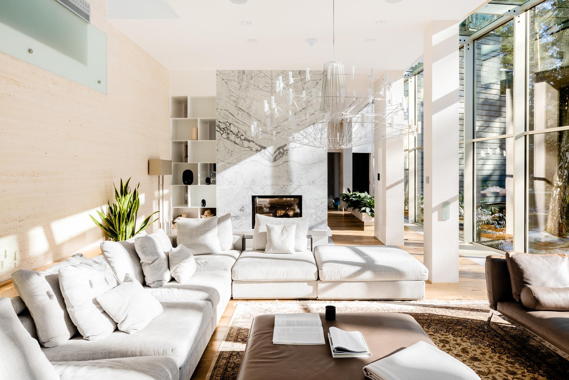 Jasny salon z marmurowym kominkiem, nowoczesnym oświetleniem i dużymi oknami. Wnętrze domu w Konstancinie Jeziornej, z przewagą bieli i naturalnego światła.