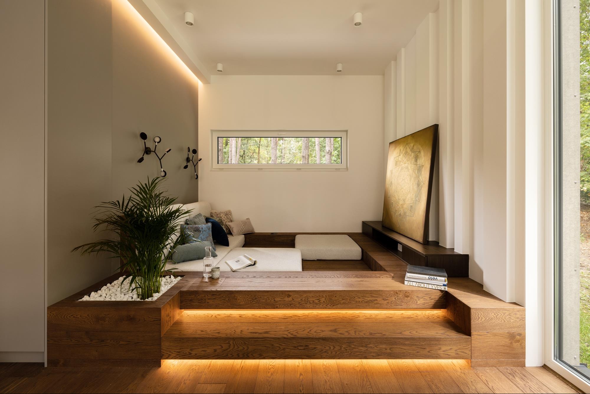 Nowoczesny salon z drewnianym podestem, oświetleniem LED i roślinami. Minimalistyczny design z oknem na las i dekoracyjnymi elementami. Przytulna aranżacja wnętrza.