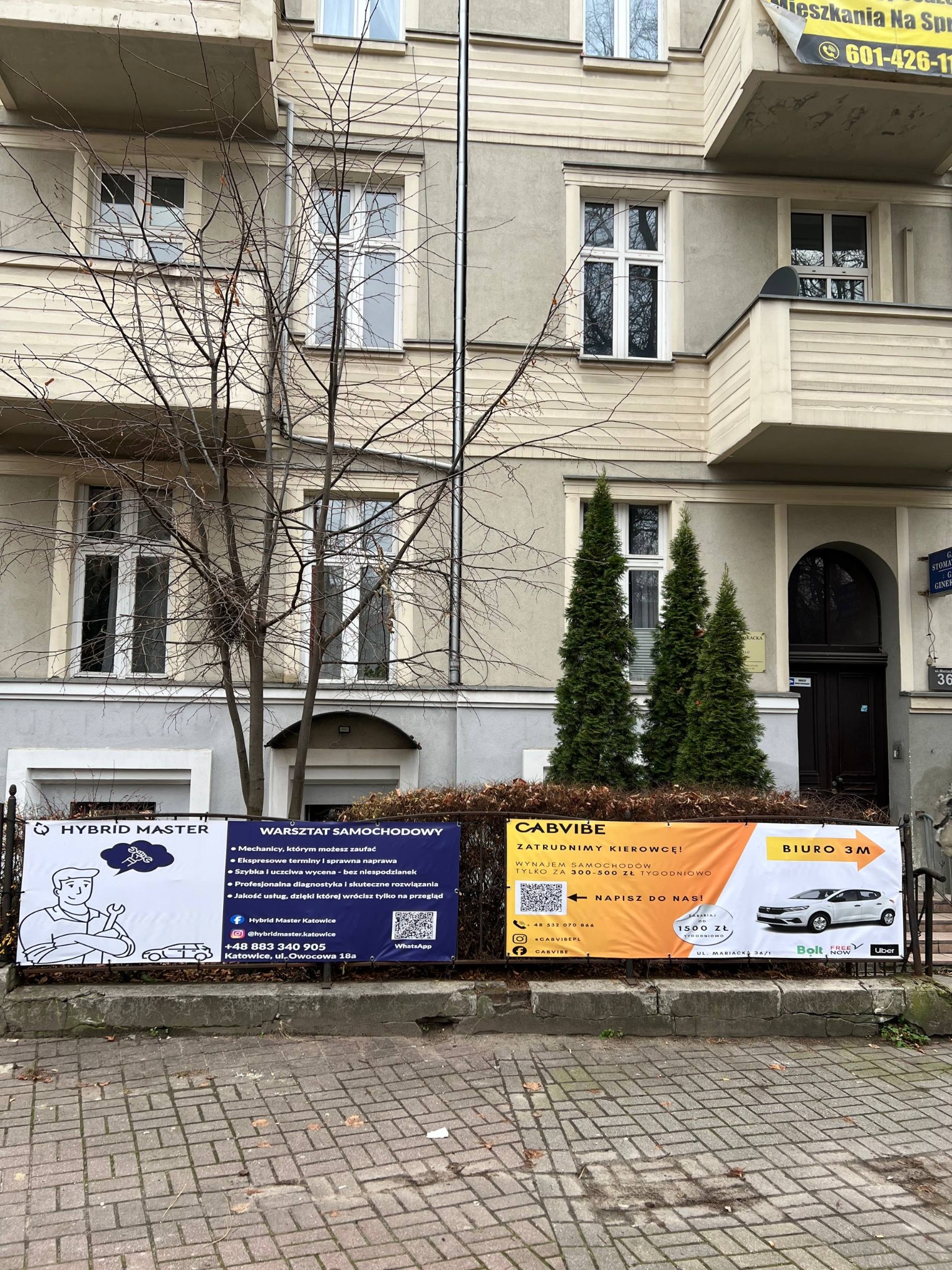 Banery reklamowe Cabvibe Taxi i warsztatu samochodowego Hybrid Master przed budynkiem w Katowicach. Oferta wynajmu aut i serwisu dla kierowców.