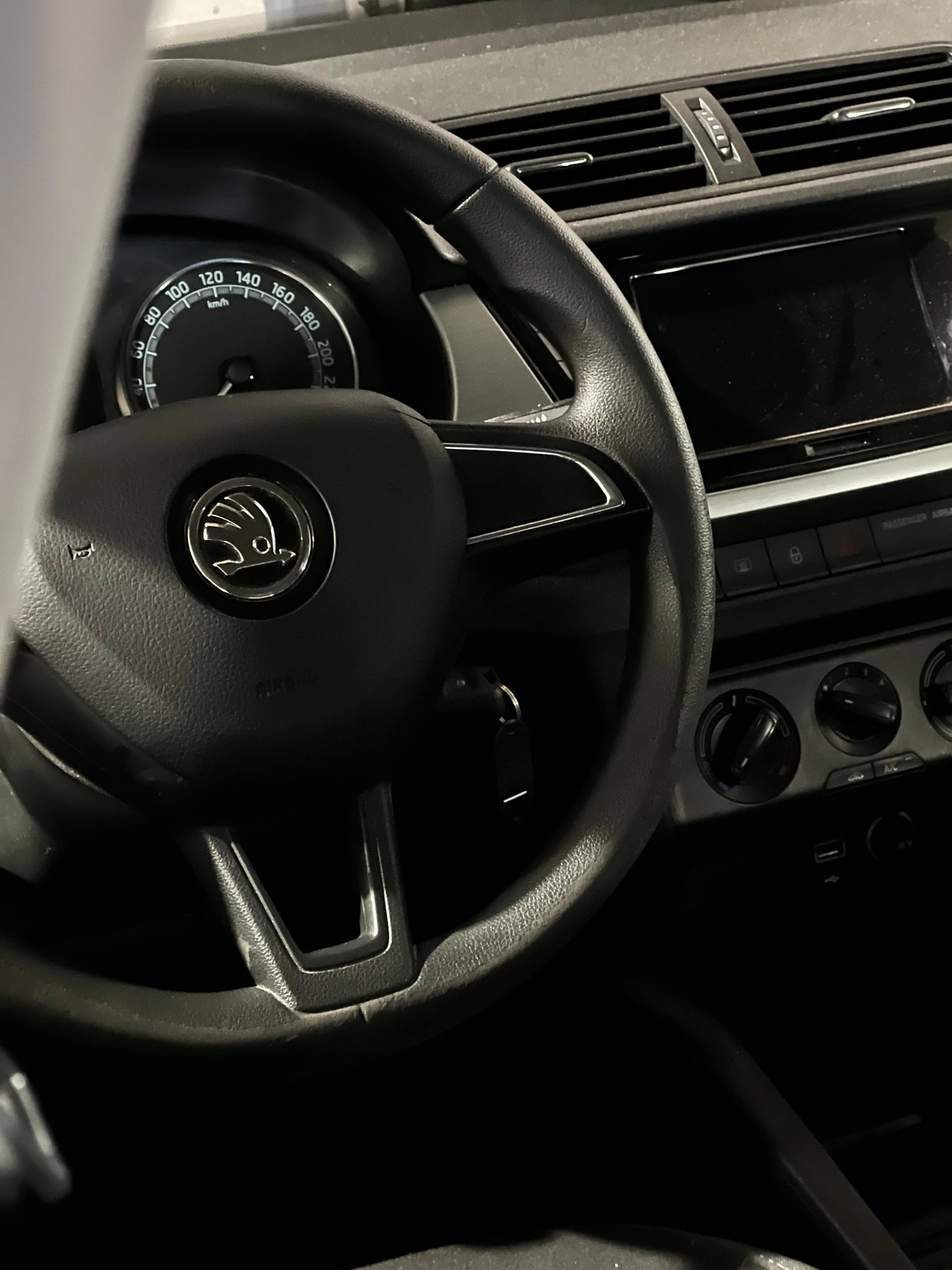 Wnętrze samochodu Skoda Fabia: kierownica z logo, deska rozdzielcza z prędkościomierzem i panelem klimatyzacji. Widoczne kluczyki w stacyjce.