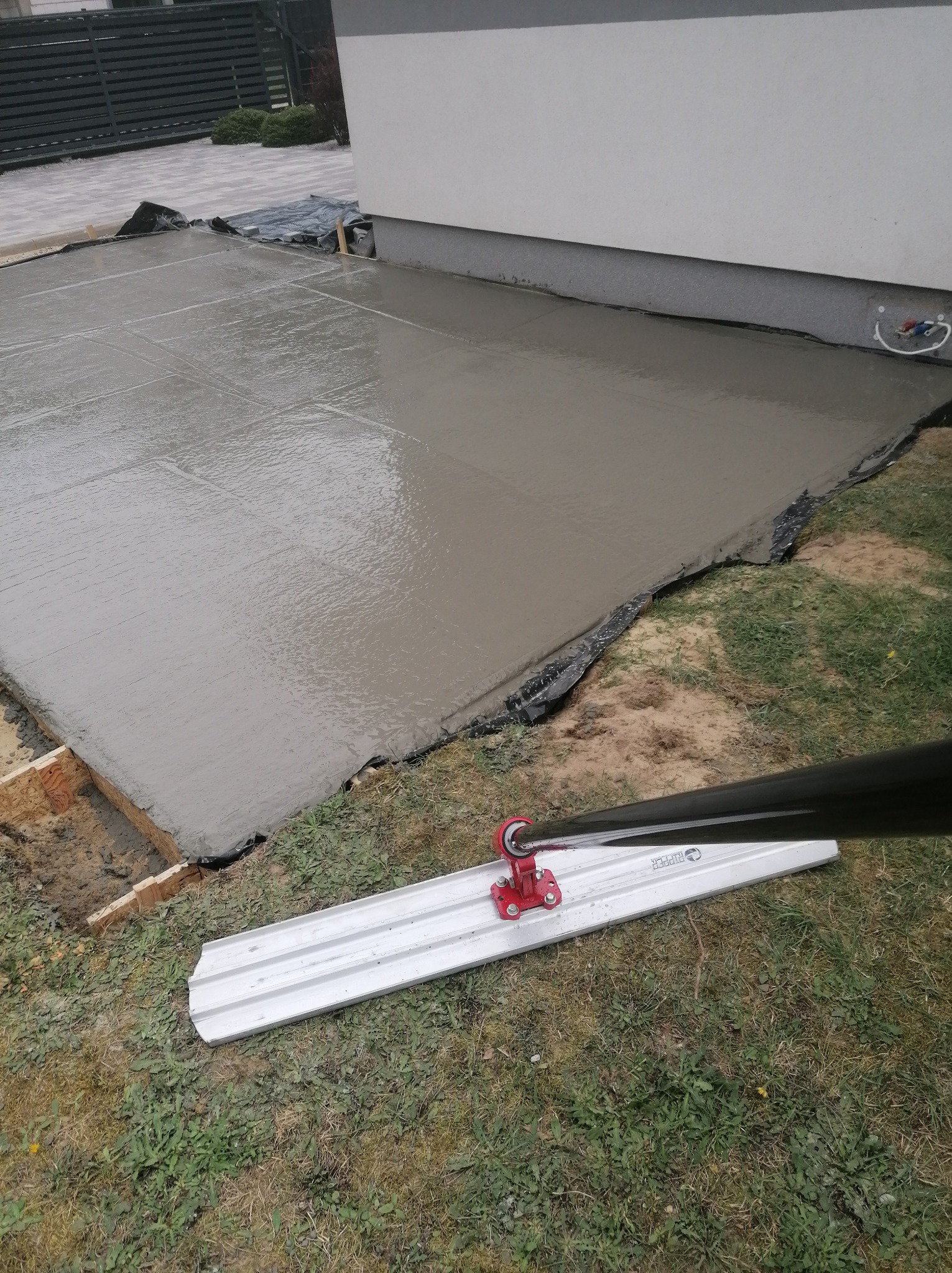 Wylany, świeży beton na fundamencie z widoczną listwą do rozprowadzania betonu. Widoczne szalunki i folia zabezpieczająca. Prace fundamentowe w toku.