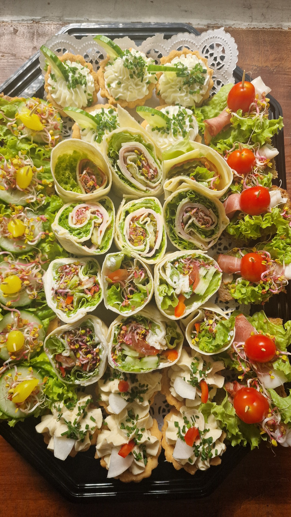 Elegancka taca z roladkami z tortilli, tartaletkami z kremem i sałatkami, udekorowana świeżymi warzywami i ziołami. Idealna na catering.