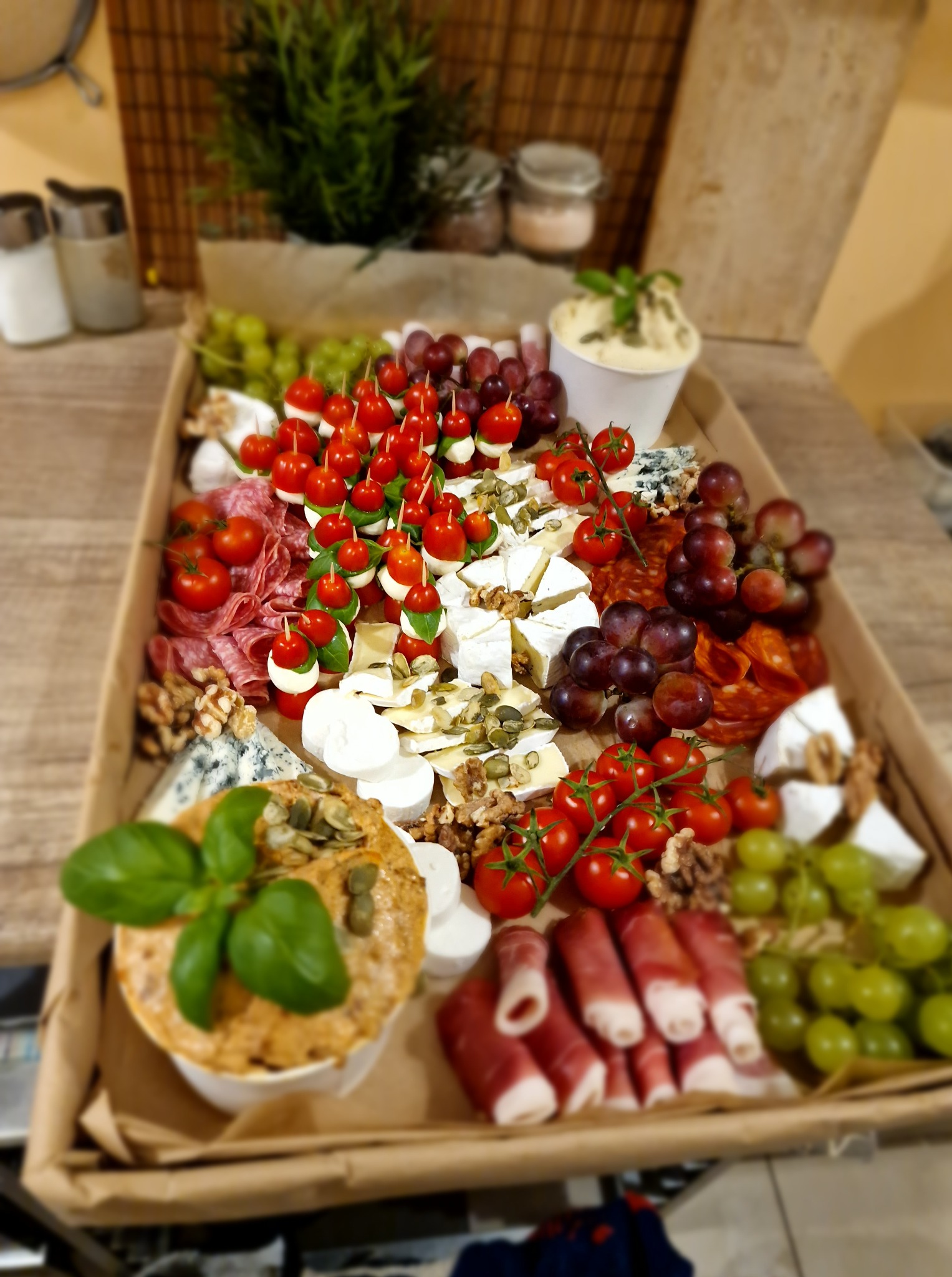 Bogato zaaranżowana deska serów i przekąsek: winogrona, pomidorki koktajlowe, mozzarella, salami, orzechy i dip, idealna na elegancki catering.