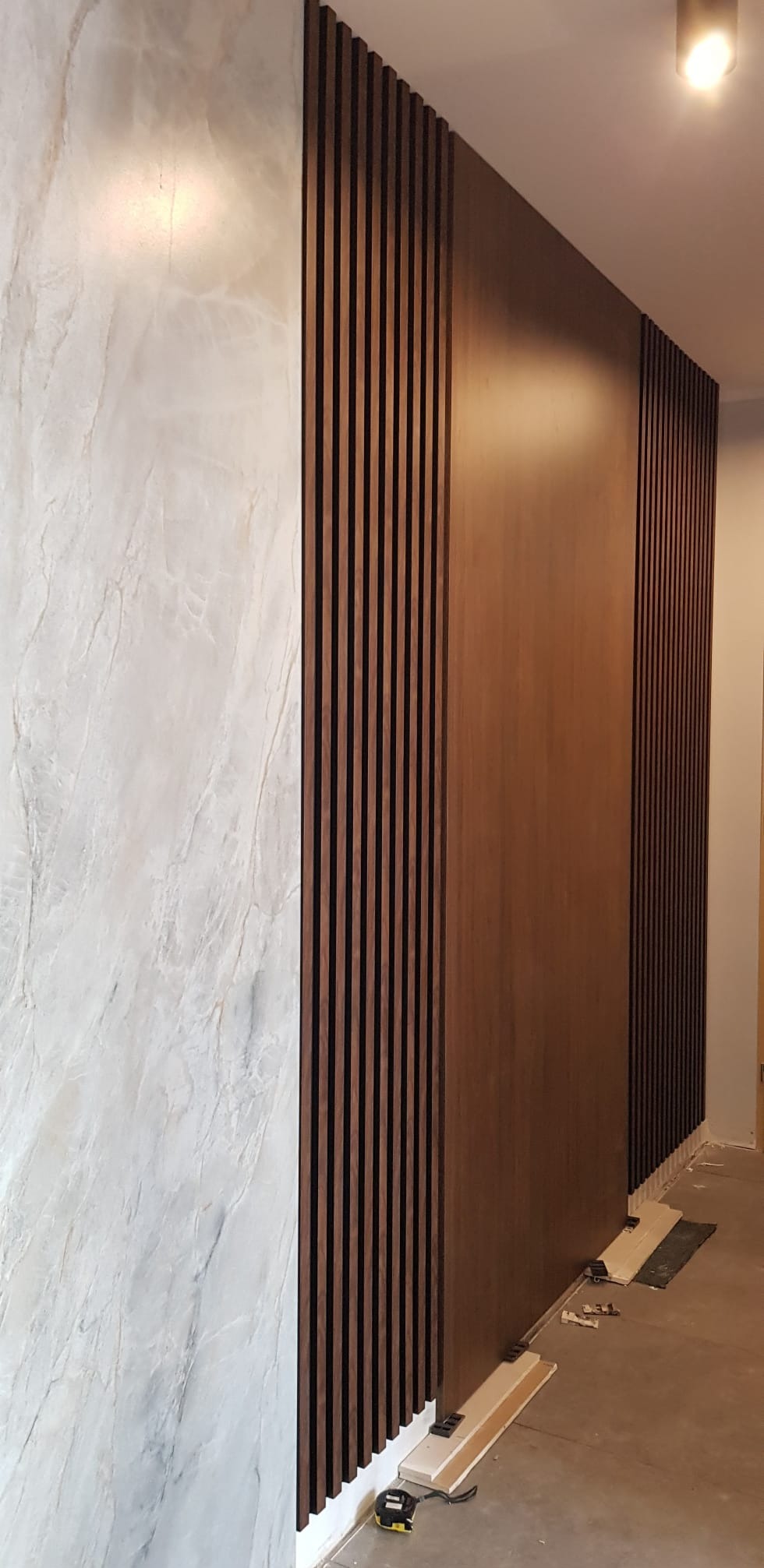 Ściana z dekoracyjnym panelem drewnianym i imitacją marmuru. Widoczne narzędzia i elementy montażowe. Wykończenie wnętrza w nowoczesnym stylu.