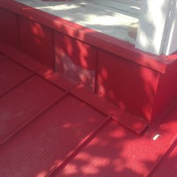 Bartosz Tomczak - Czerwony dach z blachy trapezowej, detale obróbek blacharskich przy kominie i drewnianej konstrukcji. Widoczny silikon dekarski.