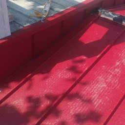 Bartosz Tomczak - Czerwony dach z blachy trapezowej, widoczne obróbki blacharskie przy kominie i narzędzia dekarskie. Ślady butów na powierzchni dachu.