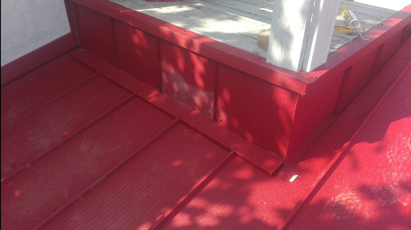 Czerwony dach z blachy trapezowej, detale obróbek blacharskich przy kominie i drewnianej konstrukcji. Widoczny silikon dekarski.